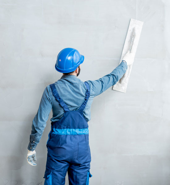 Man in blue overalls plastering a wall. Plastering services Newcastle Under Lyme